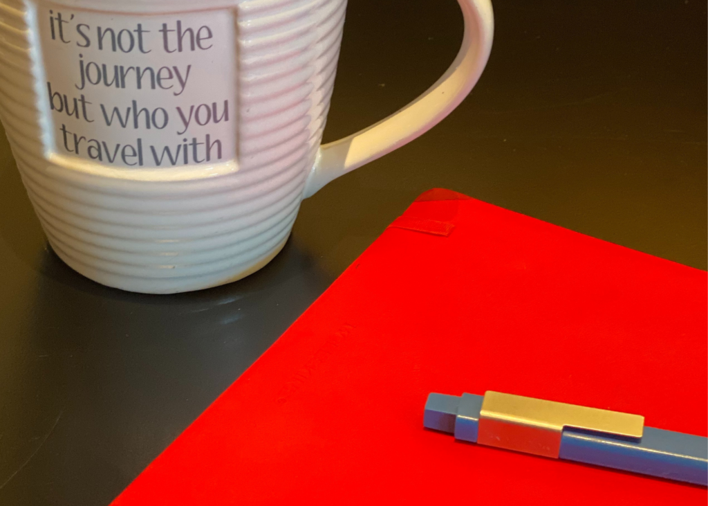 A red notebook that Karen Dukess uses for plotting, next to a mug.